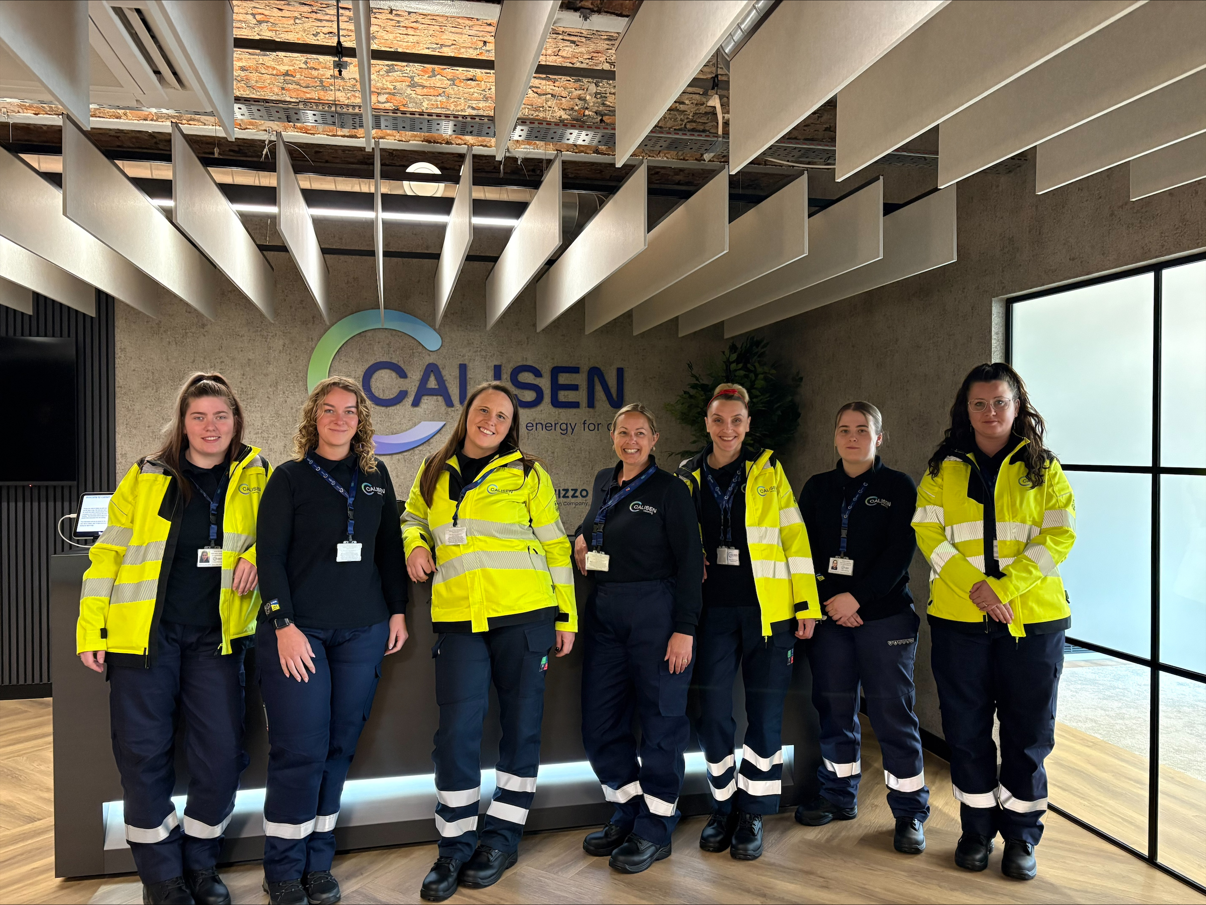 Group of eight employees in high-visibility workwear and navy uniforms standing in a reception area in front of a Calisen company logo.